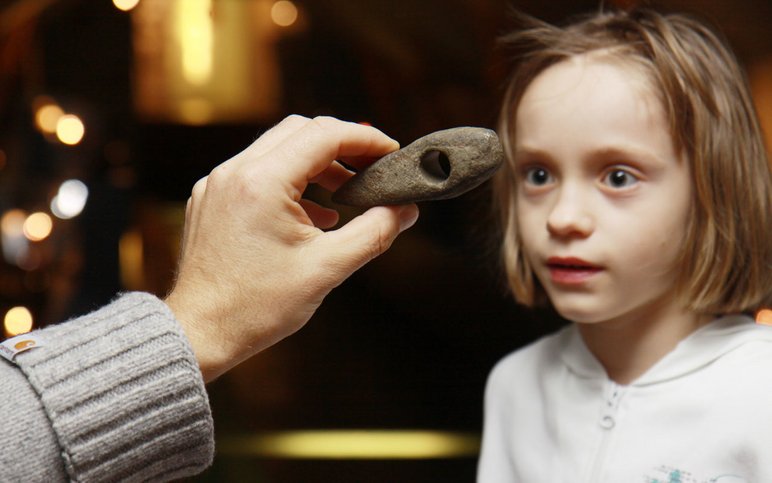 Einem Kind wird ein archäologisches Fundstück (ein Stein-Keil) gezeigt.