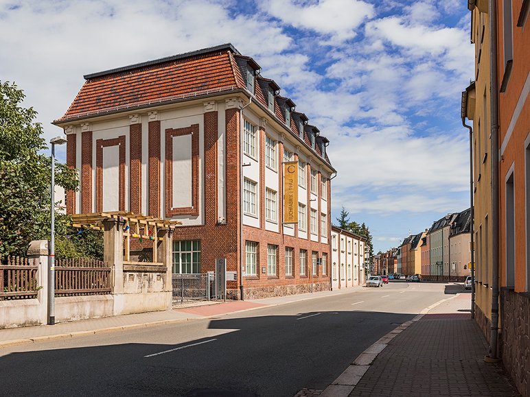 An einer beidseitig von Häusern gesäumten Straße steht ein dreistöckiges Klinkergebäude mit Kassettenfenstern.