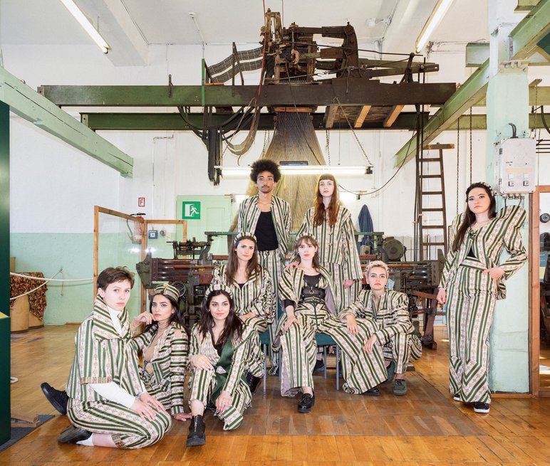 Gruppenbild junger Menschen in Kleidung aus Biedermeierstoff vor historischem Webstuhl