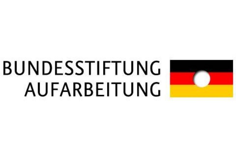 Die in Großbuchstaben geschriebenen Worte "Bundesstiftung zur Aufarbeitung" stehen links neben einer Schwarz-Rot-Goldenen Deutschlandfahne, in deren Mitte ein weißer, leerer Kreis ausgespart ist.