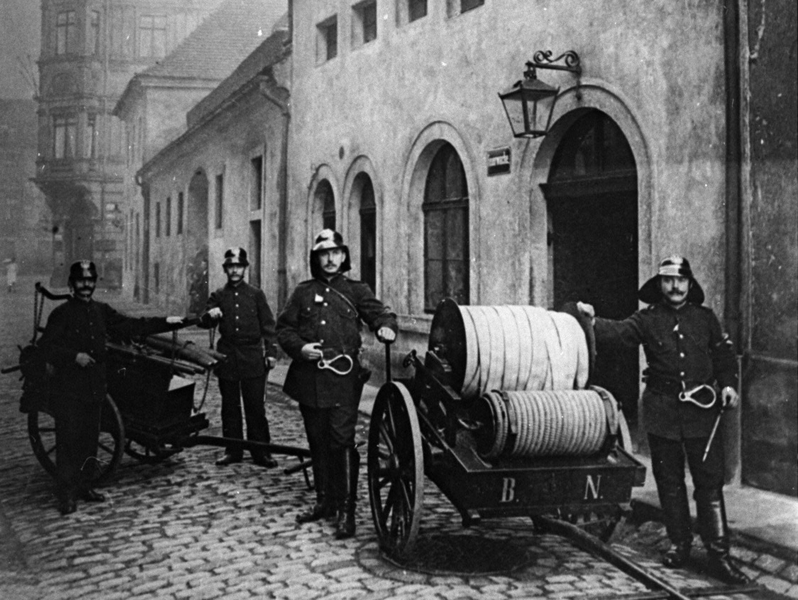 Auf dem historischen Foto sind Feuerwehrleute mit der damals typischen Löschtechnik zu sehen.
