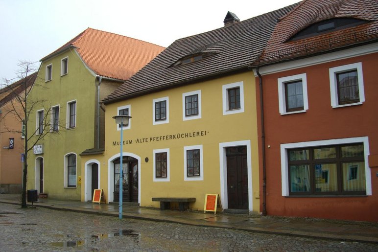 Außenansicht einer Häuserzeile mit drei historischen, zweistöckigen Gebäuden. Das Haus in der Mitte hat eine gelbe Fassade mit dem Schriftzug "Museum Alte Pfefferküchlerei".