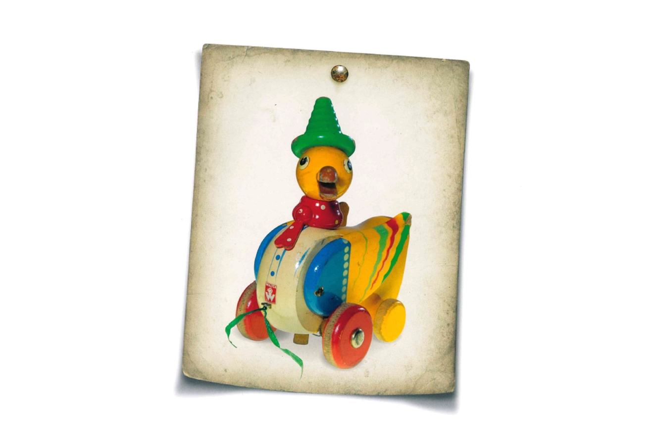 Die Abbildung zeigt ein auf einen weißen Hintergrund gepinntes Foto einer bunt bemalten Holzspielzeug-Ente mit Rädern.
